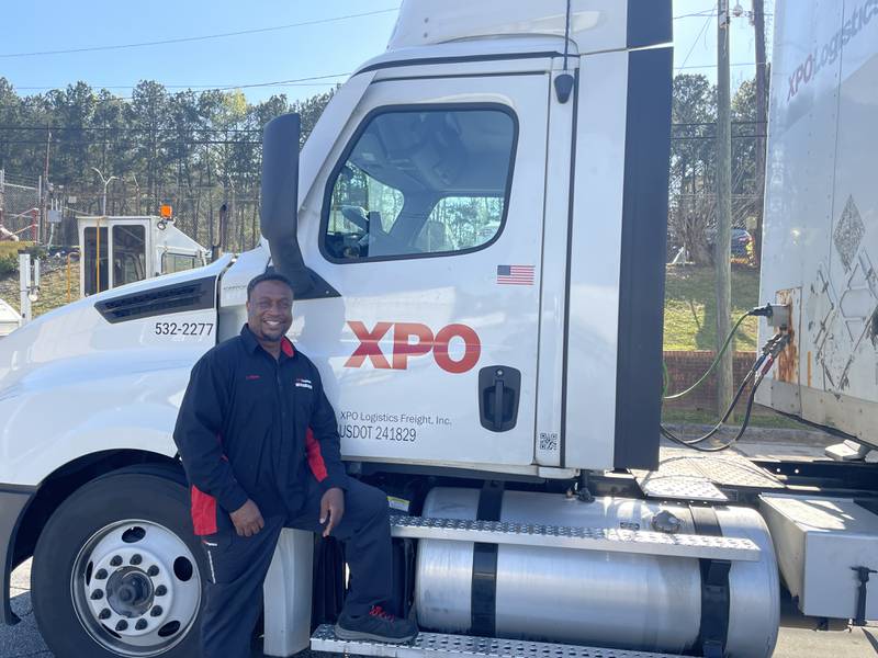 Truck driver Terry Hines poses and smiles in front of his XPO tractor trailer.