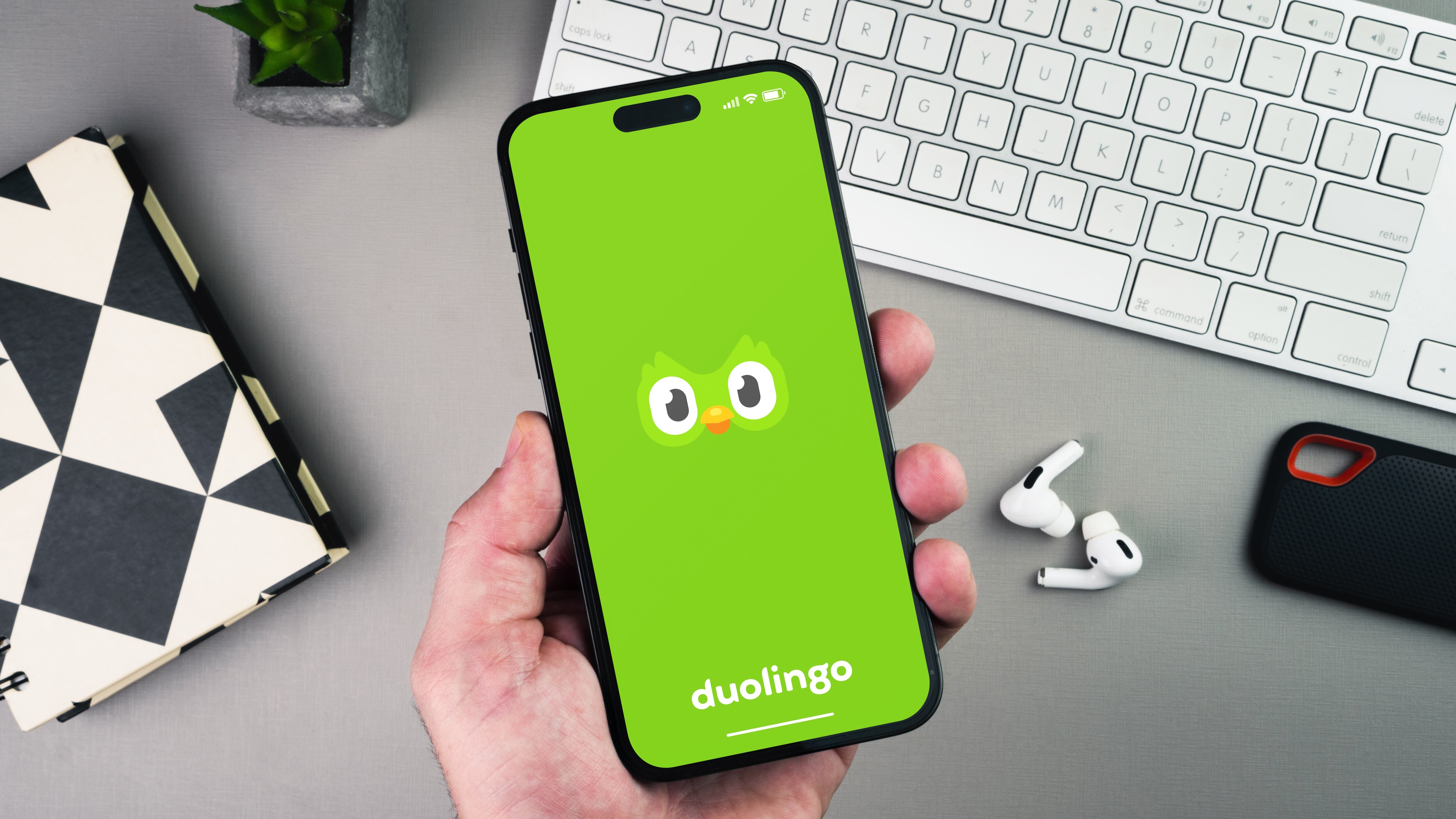 Man holding a smartphone with Duolingo language-learning on the screen on grey background table. Office environment.