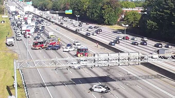Firetrucks and police shut down I-85 near Beaver Ruin Road in PM drive, sitting behind a destroyed car and large debris field.